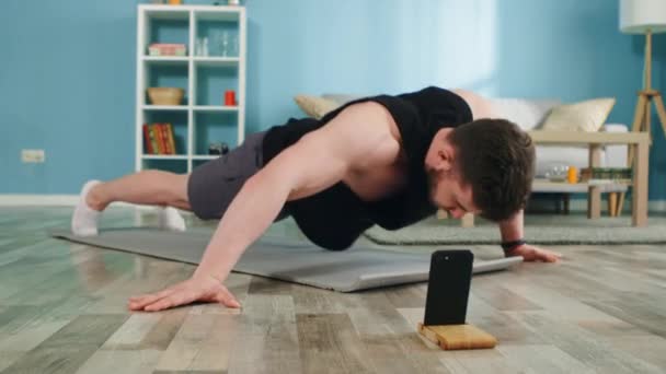 Hombre fuerte utiliza la aplicación en línea para entrenar en casa — Vídeos de Stock