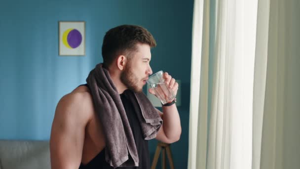 Hombre fuerte está de pie en la sala de estar y el agua potable — Vídeos de Stock