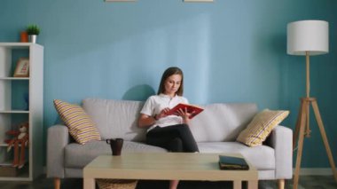 Kadın koltukta oturuyor ve kitap okuyor.
