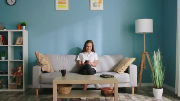 Junge Frau benutzt Handy auf Sofa sitzend — Stockvideo