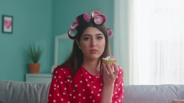 Портрет женщины с кёрлерами на голове, поедающей торт — стоковое видео