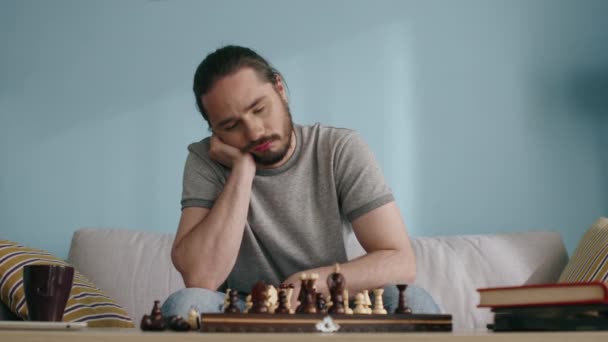 Молодой человек в самоизоляции устал играть в шахматы — стоковое видео