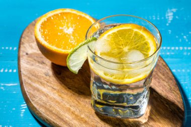 Soğuk yaz kireç ve buzlu lezzetli kuyruk beyaz ve mavi arkaplanda damla damlatan bir bardak.