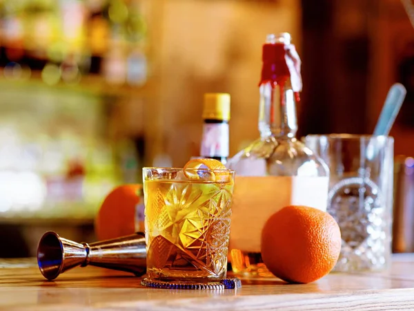 Old fashioned cocktail, orange, bottles and beaker on the bar counter