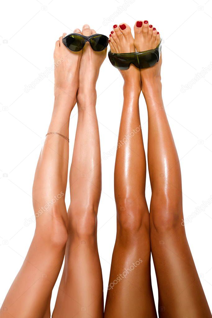 two beautiful pairs of smooth woman's legs after laser hair removal with protection glasses for laser removal on the white background