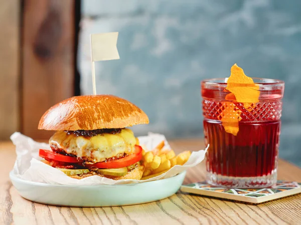 oldfashioned cocktail and fat burger with meat, cheese, tomato, pickle and french fries on the table