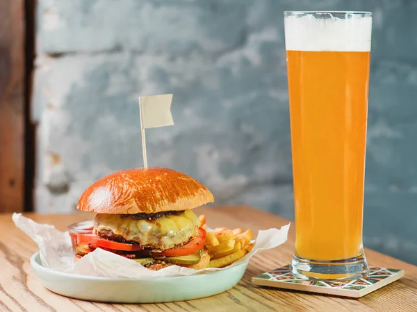 light beer and fat burger with meat, cheese, tomato, pickle and french fries on the table