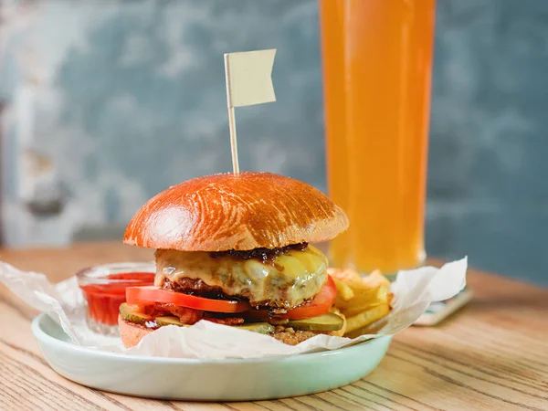 light beer and fat burger with meat, cheese, tomato, pickle and french fries on the table