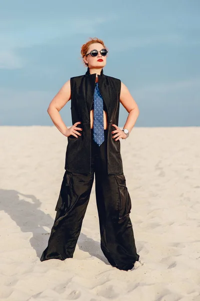 Portrait of redhead stylish woman in tie, suit and sunglasses in the desert