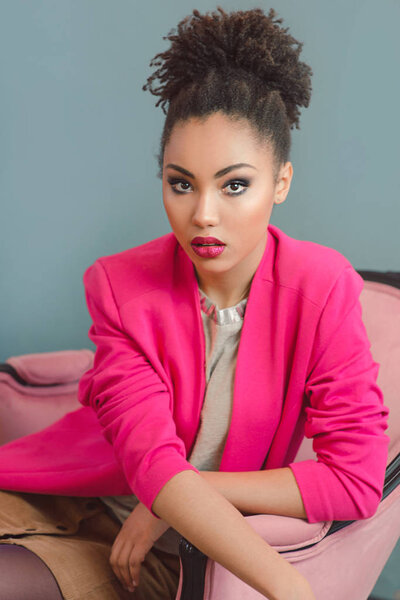 beautiful attractive young woman (mixed rase) with make up and in pink blazer sitiing on the chair