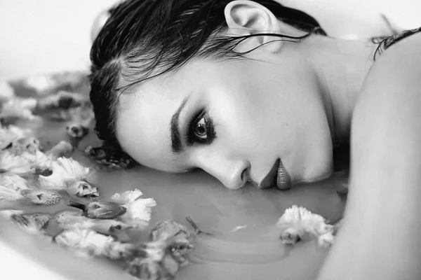 monochrome film portrait of beautiful sexy sad young slim brunette woman in bathroom with water and flowers