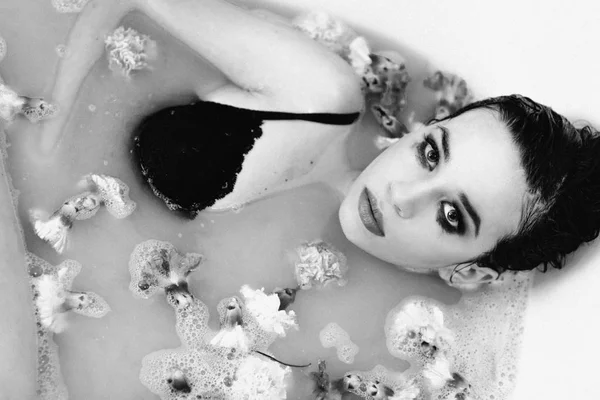 monochrome film portrait of beautiful sexy sad young slim brunette woman in bathroom with water and flowers