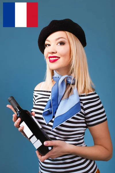 美しいブロンドの肖像フランスのベレー帽 マフラー バック 背景にフランス国旗を彼女の腕でワインとパンのバゲットのボトルと 白いシャツの女 — ストック写真