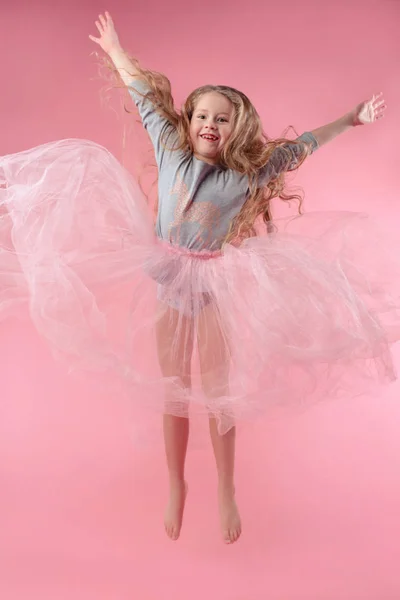 可爱有趣的小女孩与长的金发跳粉红色的背景 — 图库照片