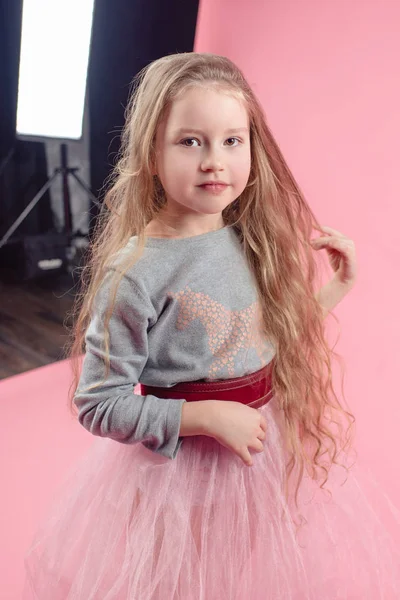 可爱的有趣的小女孩与长金发在摄影工作室在粉红色背景拍摄过程 — 图库照片