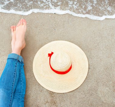 Kot beyaz kadın ayaklar yanında şapka ile sahilde deniz kenarında oturuyor. Seyahat soyut fotoğraf