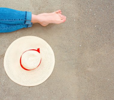 bacaklar ve kot beyaz kadın ayakları üzerinde kum arka plan tarafından yakın şapka ile sahilde deniz tarafından oturan. Seyahat soyut fotoğraf