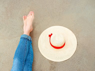 bacaklar ve kot beyaz kadın ayakları üzerinde kum arka plan tarafından yakın şapka ile sahilde deniz tarafından oturan. Seyahat soyut fotoğraf