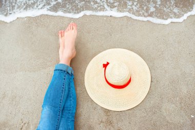 Kot beyaz kadın ayaklar yanında şapka ile sahilde deniz kenarında oturuyor. Seyahat soyut fotoğraf