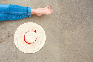 bacaklar ve kot beyaz kadın ayakları üzerinde kum arka plan tarafından yakın şapka ile sahilde deniz tarafından oturan. Seyahat soyut fotoğraf