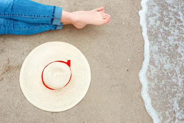 Kot beyaz kadın ayaklar yanında şapka ile sahilde deniz kenarında oturuyor. Seyahat soyut fotoğraf