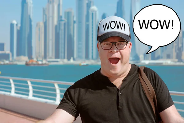 portrait of Impressed by modern Dubai (wow effect) european caucasian redhead man in glasses and hat travel to United Arabic Emirates on the cityscape, skylines and sea background in sunny day