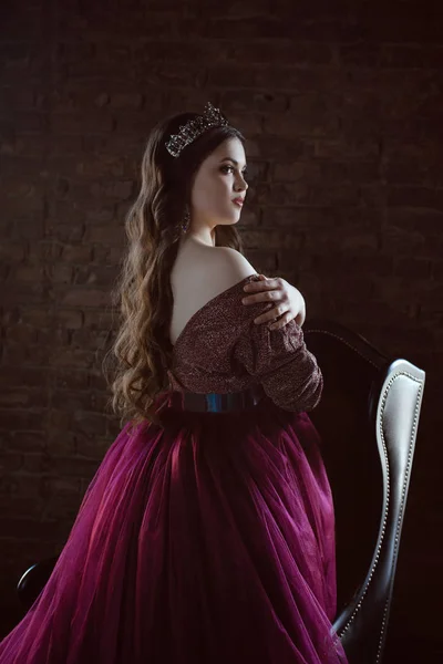 uzun saçlı uzun mor kraliçe elbise ve taç güzel genç güzel sevimli kadın prenses (kraliçe) portresi ve deri sandalye yakınında minimalist çatı iç kapalı makyaj