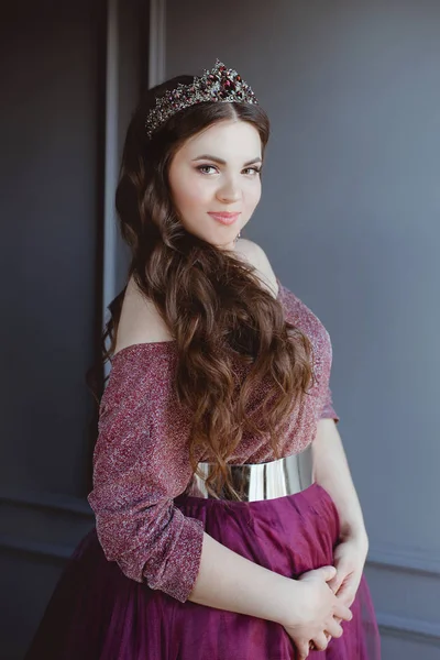 美丽的年轻漂亮可爱的女人公主 的肖像在长紫色女王的礼服和皇冠 长发和组成室内在简约的内部 — 图库照片
