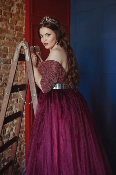 uzun saç ile uzun mor kraliçe elbise ve taç, güzel genç güzel sevimli kadın Prenses (Kraliçe) portre, kırmızı, mavi ve tuğla minimalist arka planda, iç merdivenlerde kapalı ayakta makyaj