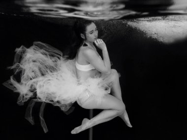 Siyah arka plan üzerinde yüzme havuzunda kutup sualtı ile beyaz elbiseli genç, fit, ince kadın Monokrom portre