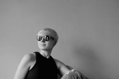 Siyah güneş gözlüğü şık sarışın genç kadın Monokrom portre, siyah gömlek ve kot duvar arka plan üzerinde yönetmen koltuğunda oturan 