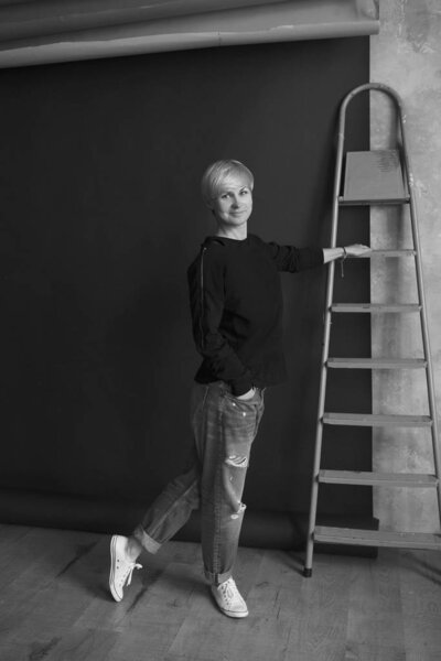 Монохромный портрет молодой блондинки современной женщины в черной толстовке и джинсах, стоящих возле лестницы и планирующих ремонт (ремонт)
) 