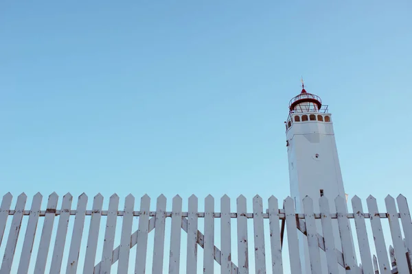 white lighthouse with white fence on blue sky background near the sea