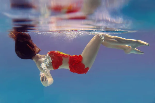 unbelievable, surreal, incredible, amazing underwater portrait of slim, fit woman in bright orange swimming suit