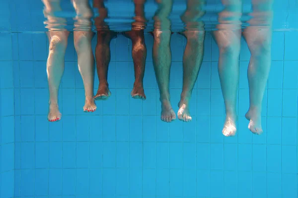 four people legs underwater in the swimming pool. Friends. Party. Summer. Vacation and sport concept.