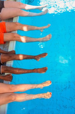 güneşli bir günde yüzme havuzunun yanında oturan dört arkadaş (sıradan insanlar) farklı ırk bacakları. Parti. Yaz. Tatil ve spor konsepti.