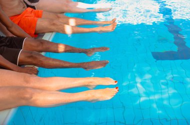 güneşli bir günde yüzme havuzunun yanında oturan dört arkadaş (sıradan insanlar) farklı ırk bacakları. Parti. Yaz. Tatil, uluslararası dostluk ve spor konsepti.