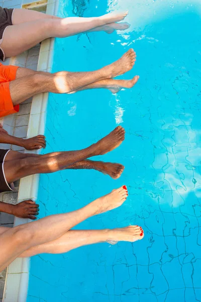 腿的四个朋友 普通人 不同种族坐在游泳池边在阳光明媚的日子 度假和运动理念 — 图库照片