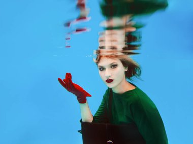 yeşil elbise, kırmızı eldiven, siyah debriyaj çantası ve yüzme havuzunda net sualtı tayt güzel şaşırtıcı şık güzel genç kadın. Moda ve alışveriş konsepti