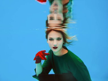 yeşil elbise, kırmızı eldiven, siyah debriyaj çantası ve yüzme havuzunda net sualtı tayt güzel şaşırtıcı şık güzel genç kadın. Moda ve alışveriş konsepti