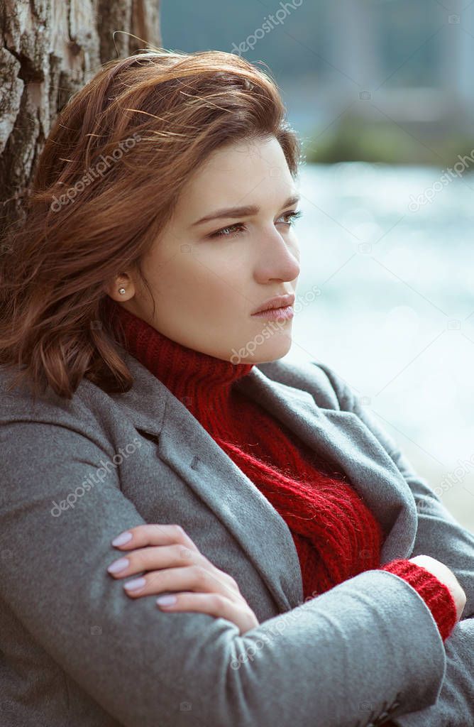 young beautiful brunette depressed sad woman by the river in the city on bridge background