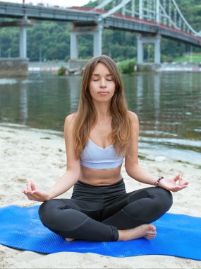 Nehrin kıyısındaki sahilde farklı yoga kıyafetleriyle gezen formda genç bir kadın. Yoga ve spor konsepti