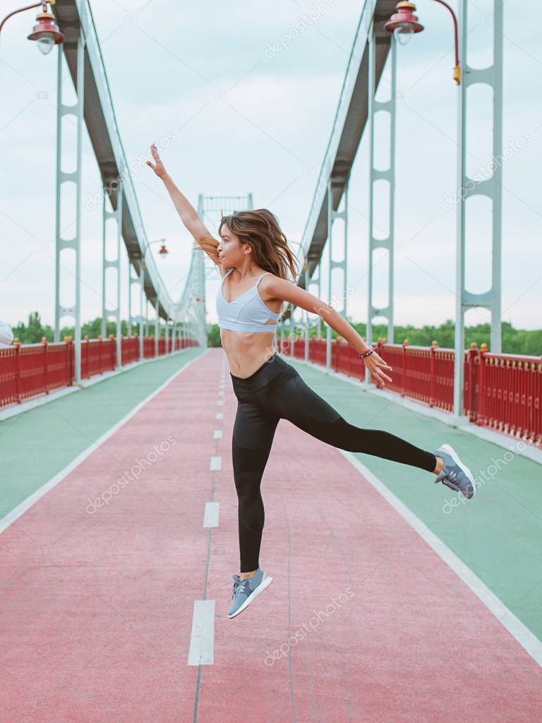 beautiful, sporty, fit, young Caucasian woman in sportswear and sneakers jumping on the bridge. Sport, activity, urban lifestyle concept
