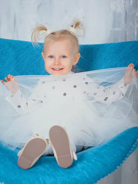 卡卡西亚快乐的小女孩 穿着时髦的白色衣服 坐在蓝色扶手椅前的画像 — 图库照片