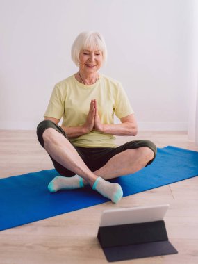 İnternette yoga yapan son sınıf neşeli, barışçıl kadın. Namaste elleri. Yaş, spor, teknoloji, yoga konsepti