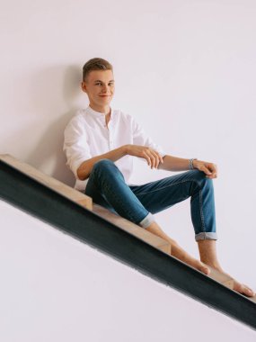 Beyaz gömlekli ve mavi kotlu yakışıklı adam kapalı bir merdivende oturuyor. Moda, tarz kavramı