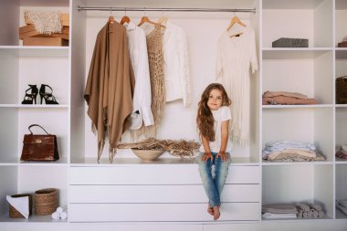 Beyaz tişörtlü ve kot pantolonlu komik küçük kız yetişkin ve modaya uygun olmayı hayal ediyor. Yaş, çocukluk, moda, tarz kavramı