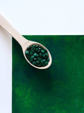 Yeşil Hawaii spirulinası yemek kaşıklarında haplar tahta kaşıkta yeşil arka planda. Süper yemek, sağlıklı yaşam tarzı, sağlıklı takviyeler, aşçılık konseptinde süper yiyecekler.