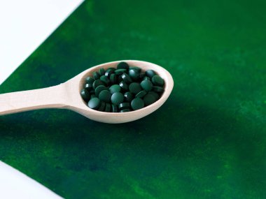 Yeşil Hawaii spirulinası yemek kaşıklarında haplar tahta kaşıkta yeşil arka planda. Süper yemek, sağlıklı yaşam tarzı, sağlıklı takviyeler, aşçılık konseptinde süper yiyecekler.