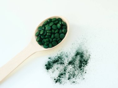 Masa kaşıklarıyla yeşil Hawaii spirulinası hapları ve açık beyaz arka planda toz. Süper yemek, sağlıklı yaşam tarzı, sağlıklı destek konsepti.